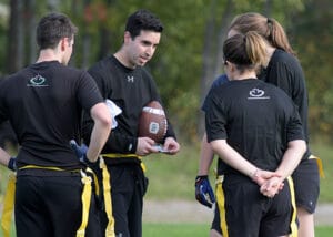 Two guys and two girls in a huddle discussing flag football plays.